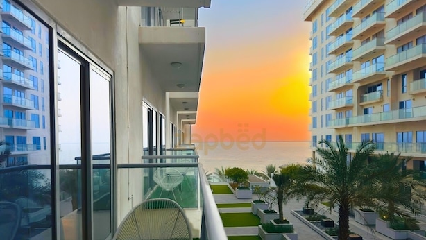 A balcony with a view of a sunset, a palm tree, and a chair. - RAK F 202 (Ras Al Khaimah)