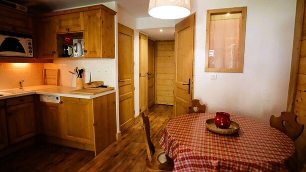 Cocina compacta con armarios de madera, microondas y un comedor con mantel a cuadros.