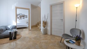 Un salon moderne avec un canapé gris, une petite table ronde sur laquelle repose un livre, un vase contenant des plantes séchées et une lampe.