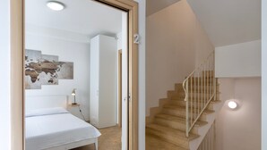 Une chambre à coucher comprenant un lit, une table de chevet, une lampe fixée au mur et un escalier muni d’une rampe.