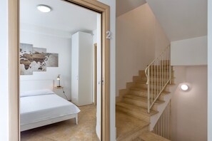 A bedroom with a bed, a nightstand, a wall-mounted lamp, and a staircase with a railing.