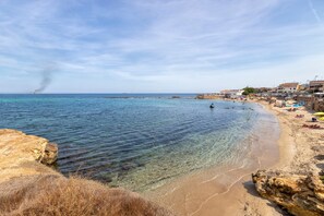 A beach with clear water, rocky shore, and buildings in the background. - Room 'L'Angolo- Camera 3' with Shared Terrace, Wi-Fi and Air Conditioning (Porto Torres)