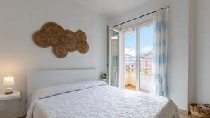 Une chambre à coucher comprenant un lit, une lampe de chevet, un objet décoratif fixé au mur et une vue sur l’extérieur, visible à travers une porte vitrée.