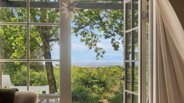 Una stanza con una grande finestra che si affaccia su una terrazza e una vista panoramica di alberi e uno specchio d'acqua.