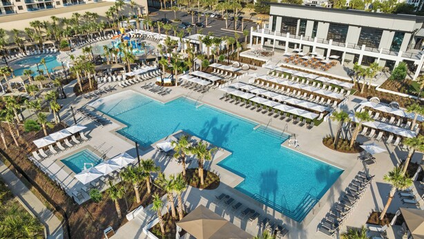 Ovenfra set et resort med flere swimmingpools, liggestole og palmer.