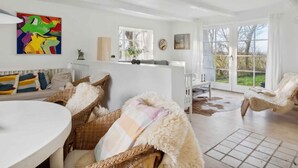 A spacious living room with a white sofa, a dining table, and wicker chairs. There is a colorful abstract painting on the wall and a window with a view of the outdoors. - 5 Star Holiday Home in Nykobing M (Nykobing Mors)