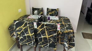 A dining table with a black and gold patterned tablecloth, two matching pillows, a water bottle, and a set of cutlery. - CC Elite Homestay (Hyderabad)