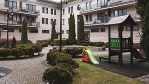 Un cortile con un’area giochi, che include uno scivolo e una panchina, circondato da siepi curate e un percorso in pietra.