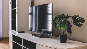 Una TV a schermo piatto su un mobile bianco con una pianta in vaso accanto.