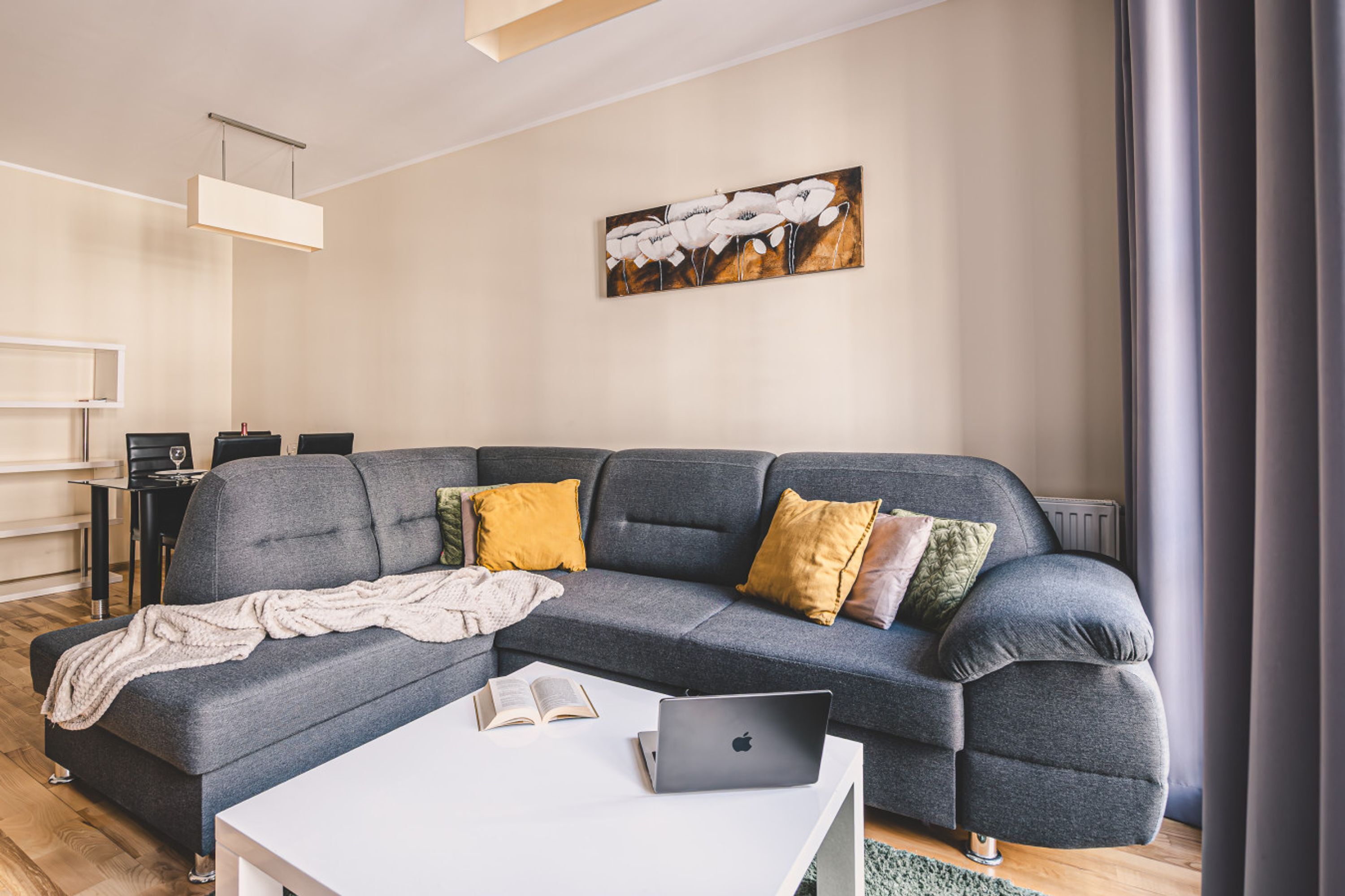 A modern living room with a grey sectional sofa, a white coffee table, and a laptop.
