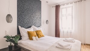 Una camera d'albergo moderna con un letto grande, una pianta in vaso e vista sulla città attraverso tende leggere.
