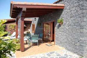 A stone building with a covered patio, outdoor furniture, and a glass door. - Charming Casa Cabrera with stunning sea views and spacious terrace (Fuencaliente de La Palma)