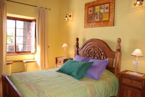 A bedroom with a wooden bed, a window with curtains, a nightstand, and a wall-mounted light fixture. - Charming Casa Cabrera with stunning sea views and spacious terrace (Fuencaliente de La Palma)