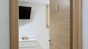 A room with a wooden door, a white dresser, a small plant, and a mounted television. - Studio Apartment 'L'Angolo Monolocale- Porto Torres' with Shared Terrace, Wi-Fi and Air Conditioning (Porto Torres)