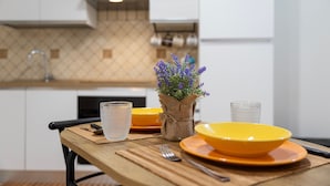 A dining table with yellow plates and a clear glass, a fork, and a vase with purple flowers. - Studio Apartment 'L'Angolo Monolocale- Porto Torres' with Shared Terrace, Wi-Fi and Air Conditioning (Porto Torres)