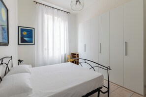 Een slaapkamer met een bed, nachtkastje, stoel, kledingkast en een schilderij aan de muur.