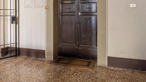 An arched doorway with a metal grill, a dark wooden door, and a light fixture above it. - Montegrappa Apartment by Wonderful Italy (Bologna)