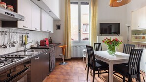 A modern kitchen with a gas stove, sink, and various utensils. There is a dining table with chairs and a vase of flowers. A television is mounted on the wall above the table. - Montegrappa Apartment by Wonderful Italy (Bologna)