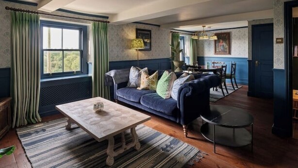 Una sala de estar acogedora con un sofá azul, una mesa de centro de madera y un comedor con mesa y sillas.