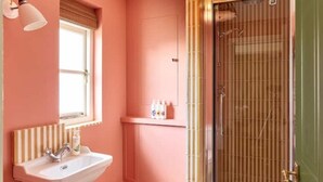 Un baño con pared rosa, un lavabo con toallero a rayas y una ducha con puerta de cristal.