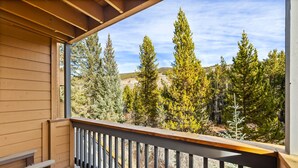 Un balcon en bois offrant une vue sur de grands arbres à feuilles persistantes et un ciel dégagé.