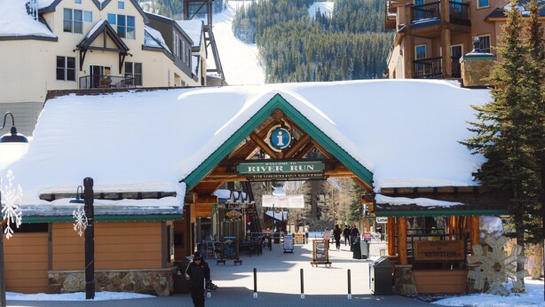 L’entrée d’une station de ski, avec une pancarte en bois indiquant « River Run », et un paysage enneigé en arrière-plan.