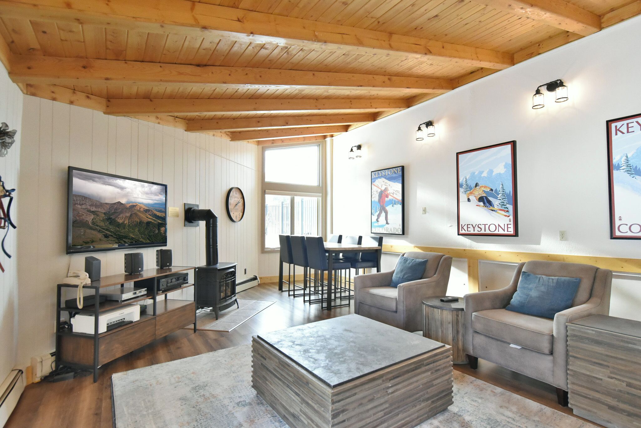 Una sala de estar acogedora con techo de madera, chimenea, televisor y comedor con sillas y mesa.