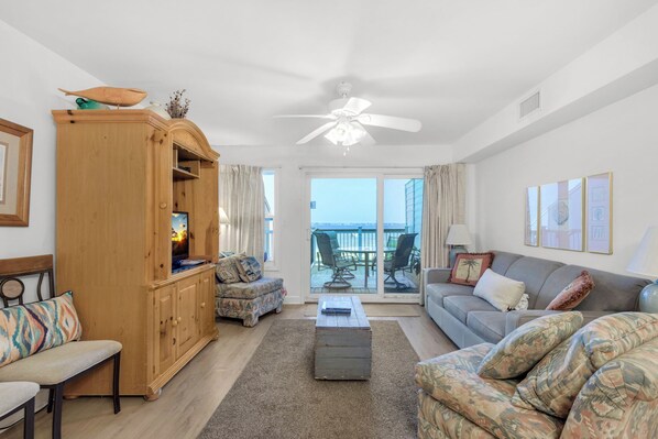 A spacious living room with a wooden cabinet, a sofa, a coffee table, and a view of the balcony. - 🐚🌴Bayfront San De Luna #2 | Balcony, Pool Access + Steps to Gulf 🐚 (Pensacola Beach)