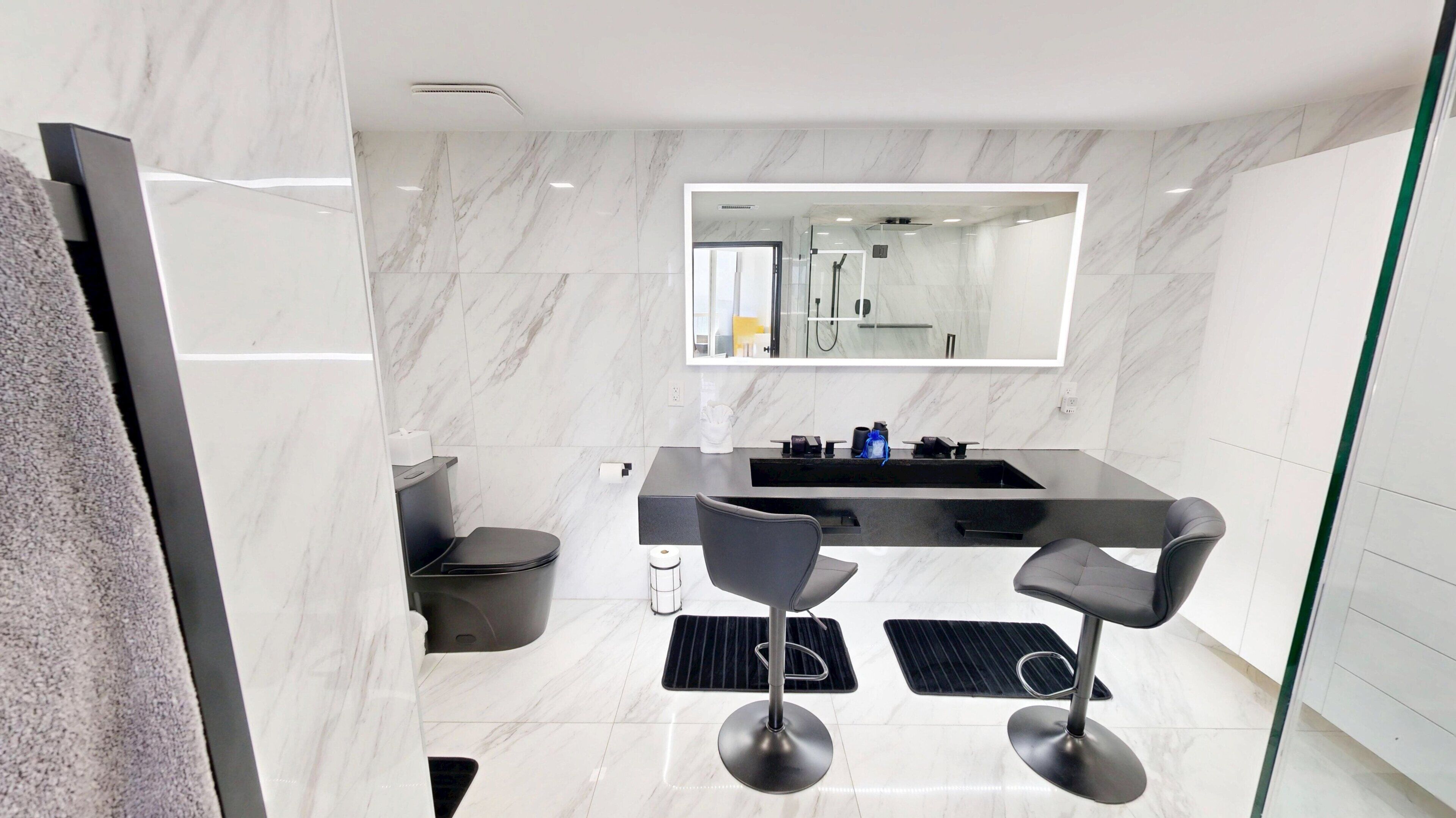A modern bathroom with a marble floor, a large mirror, a black sink, and two bar stools.