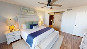 Un dormitorio con una cama grande, dos mesitas de noche con lámparas, un ventilador de techo, un armario de madera y una puerta corredera estilo granero.