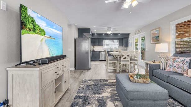 A modern kitchen with a refrigerator, a dining area with a table and chairs, and a living room with a sofa and a TV. - 171 Canal Cove: 2br W/ Canal Views 2 Bedroom Home (Fort Myers Beach)