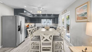 A modern kitchen with a large island, dark cabinets, and a stainless steel refrigerator. - 171 Canal Cove: 2br W/ Canal Views 2 Bedroom Home (Fort Myers Beach)