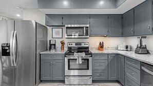 A modern kitchen with grey cabinets, stainless steel appliances, and a granite countertop. - 171 Canal Cove: 2br W/ Canal Views 2 Bedroom Home (Fort Myers Beach)