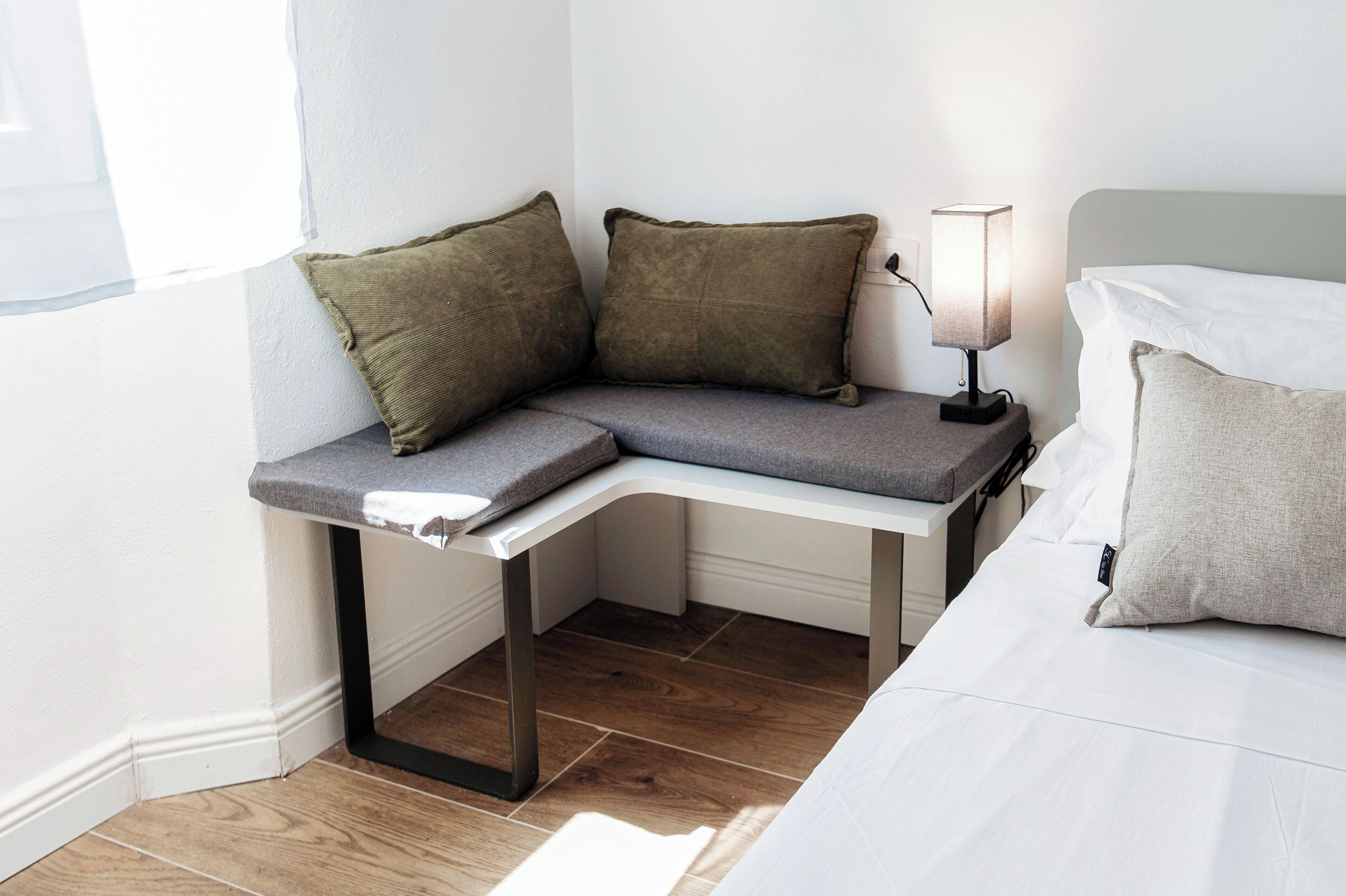 A corner bed with a nightstand, a lamp, and two pillows.