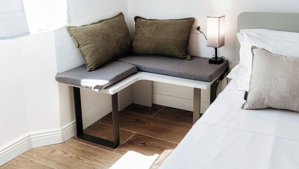 A corner bed with a nightstand, a lamp, and two pillows. - Batèl House 1 - By Breva Collections (Como)