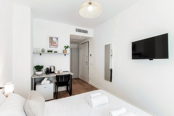 Une chambre d’hôtel moderne équipée d’un lit, d’un bureau avec un ordinateur, d  ’une télévision et d’un petit réfrigérateur.