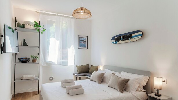 A modern hotel room with a neatly made bed, a bedside table with a lamp, a wall-mounted TV, and a window with sheer curtains. - Batèl House 1 - By Breva Collections (Como)