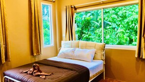 A bedroom with a bed, a window with curtains, an air conditioner, and a view of greenery outside. - Lucky Sky Homestay (Ko Pha-ngan)