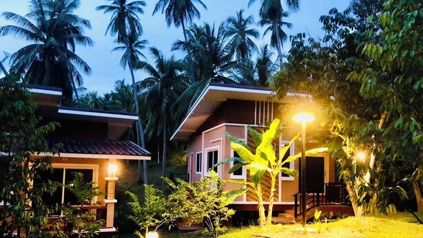 A bungalow with a tiled roof, surrounded by lush greenery and palm trees. - Lucky Sky Homestay (Ko Pha-ngan)