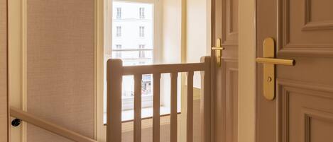 A hallway with a wooden railing, a door with a handle, and a light switch on the wall.