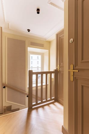 Ein Korridor mit Holzbalkon, einer Tür mit Griff und einem Lichtschalter an der Wand.