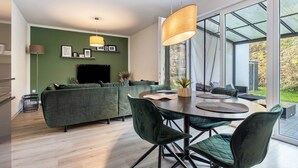 A modern living room with a green sofa, a dining table with chairs, and a large window with a view of the outdoors. - Apartment 'Altenbeken-2' with Private Terrace, Private Garden and Wi-Fi (Altenbeken)