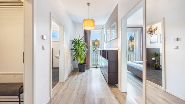 A modern hallway with wooden flooring, a potted plant, a pendant light, and a bed in the adjacent room. - Apartment 'Altenbeken-2' with Private Terrace, Private Garden and Wi-Fi (Altenbeken)