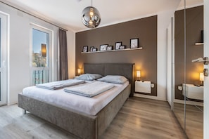 Quarto moderno com uma cama grande, mesas de cabeceira, um espelho e uma estante na parede com quadros.