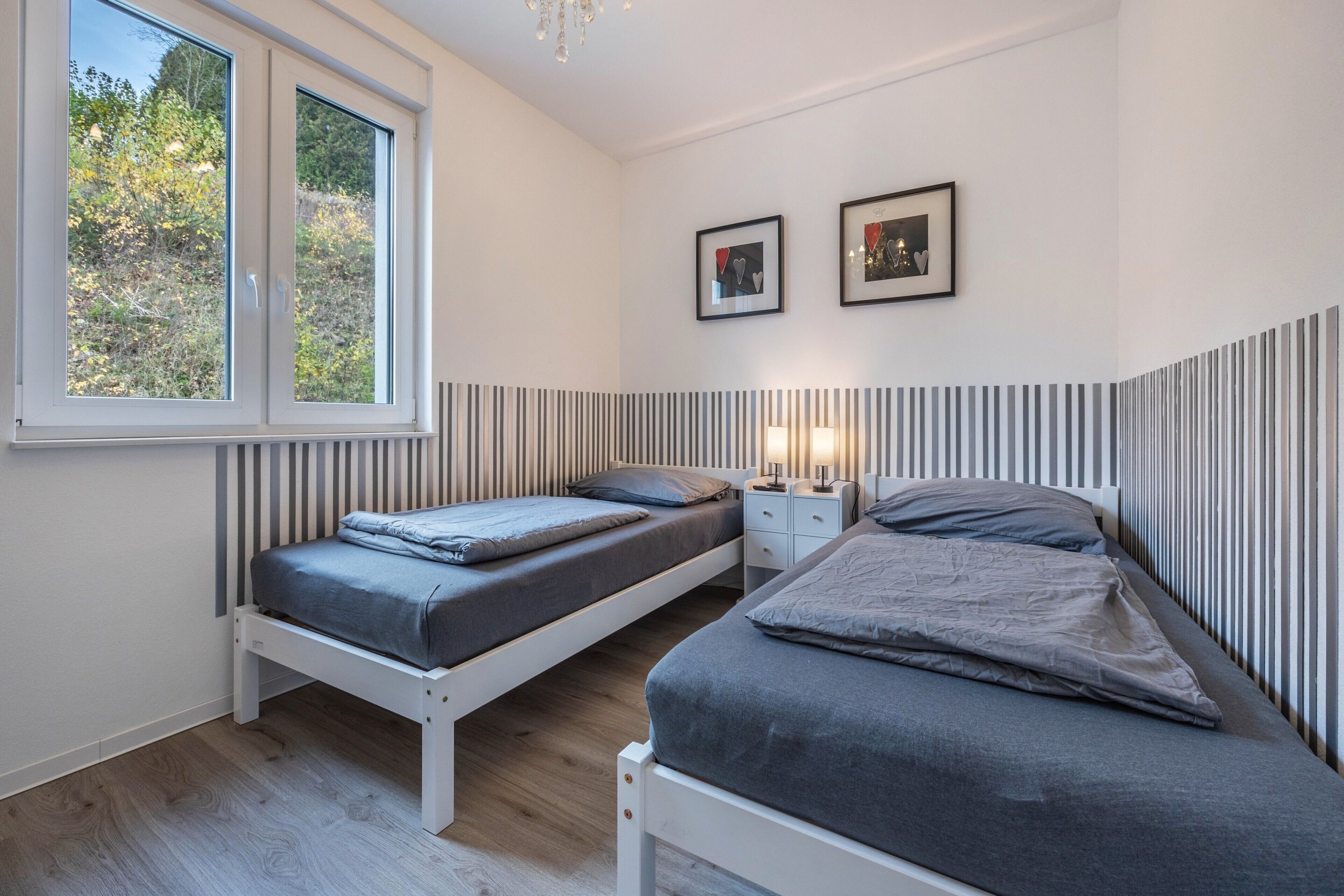A bedroom with two beds, a window, and a wall-mounted light fixture.