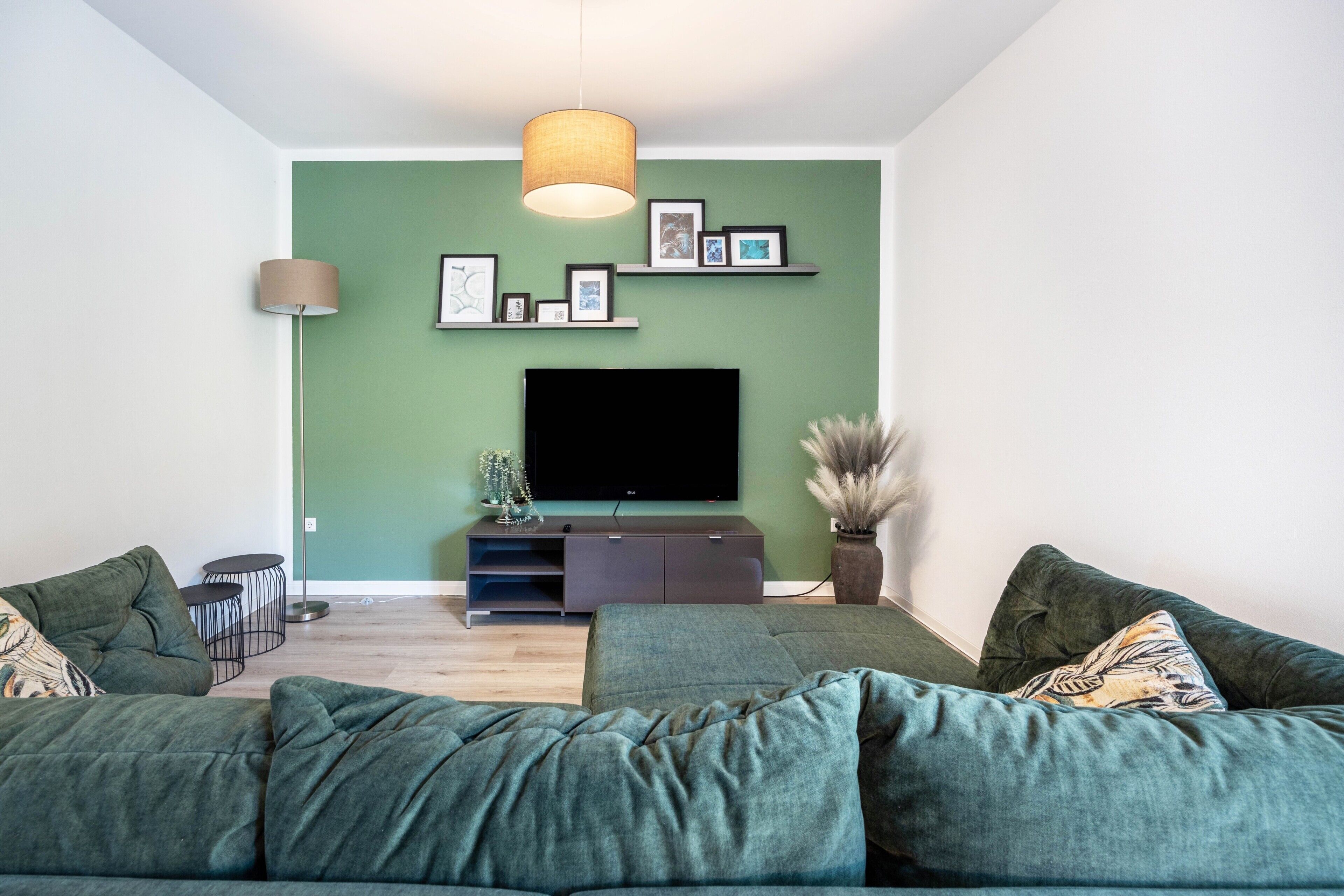 A modern living room with a green wall, a flat-screen TV, a sofa, and a lamp.