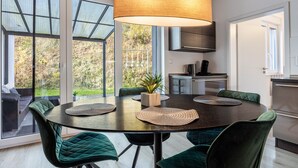 A modern dining area with a round table, green upholstered chairs, and a large pendant light. - Apartment 'Altenbeken-2' with Private Terrace, Private Garden and Wi-Fi (Altenbeken)