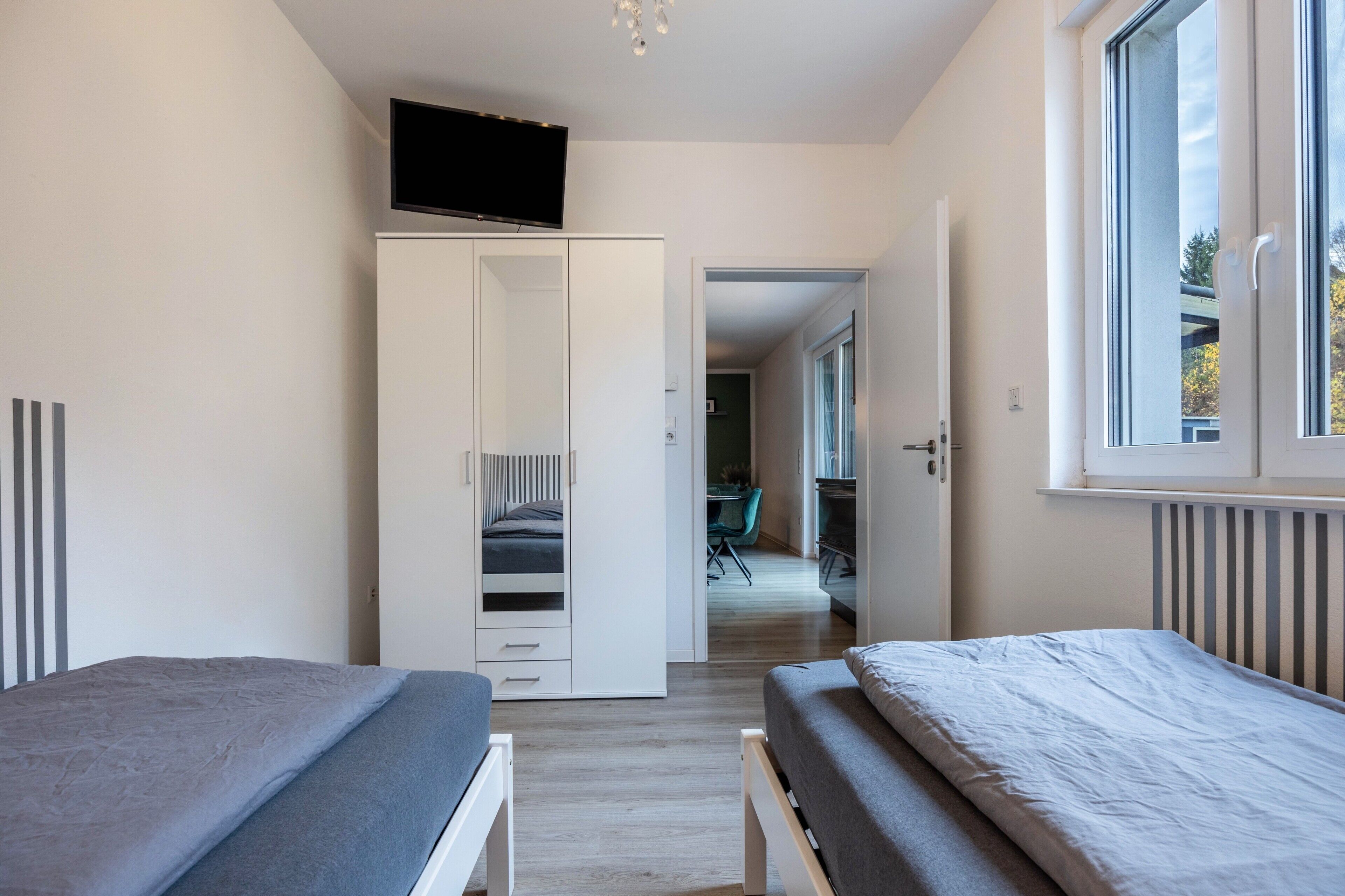 A bedroom with two beds, a wardrobe, a TV, and a window.