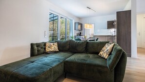 A modern living room with a sectional sofa, a kitchen in the background, and large windows. - Apartment 'Altenbeken-2' with Private Terrace, Private Garden and Wi-Fi (Altenbeken)