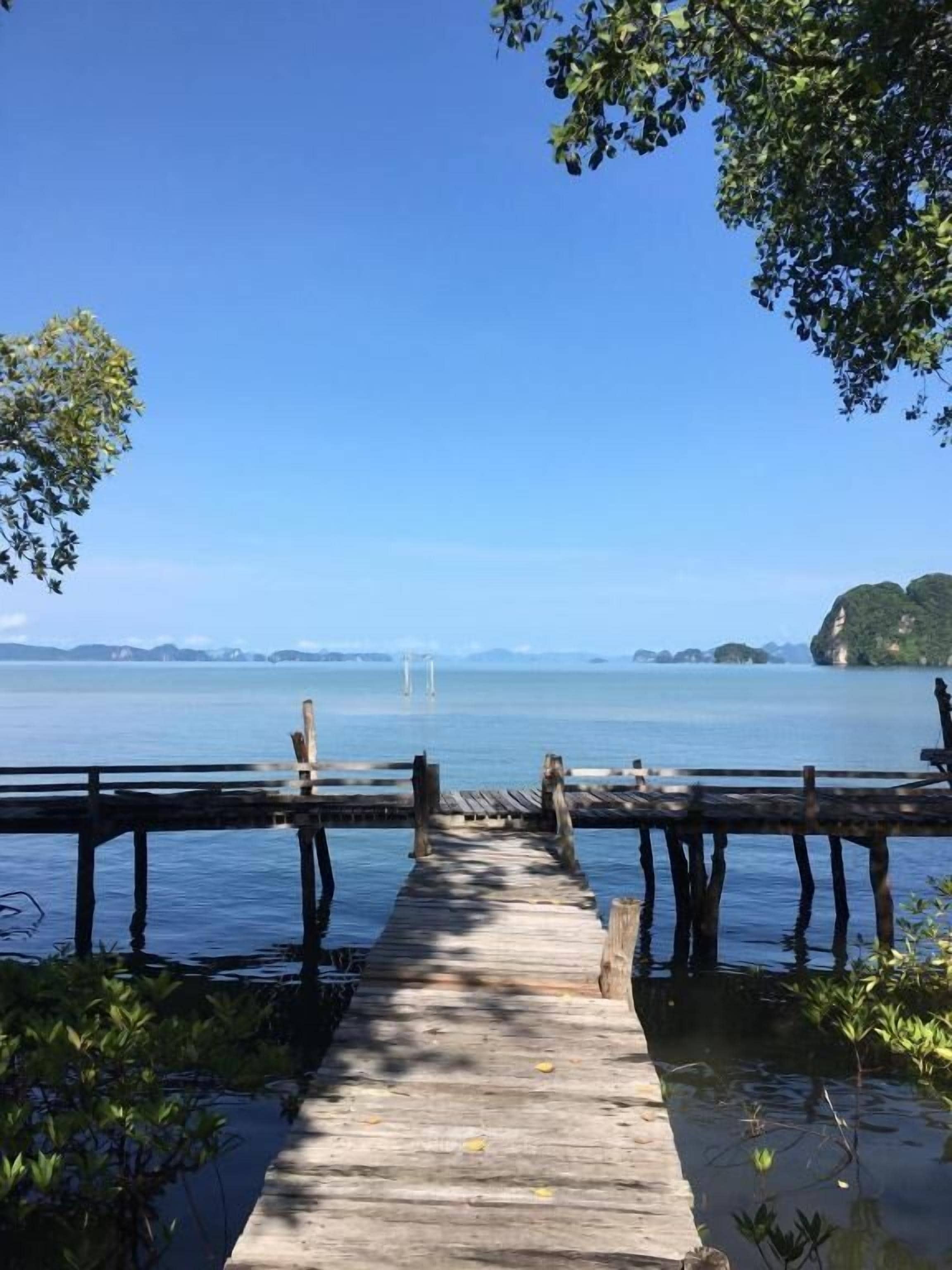 A wooden pier leading to a calm body of water with distant islands.